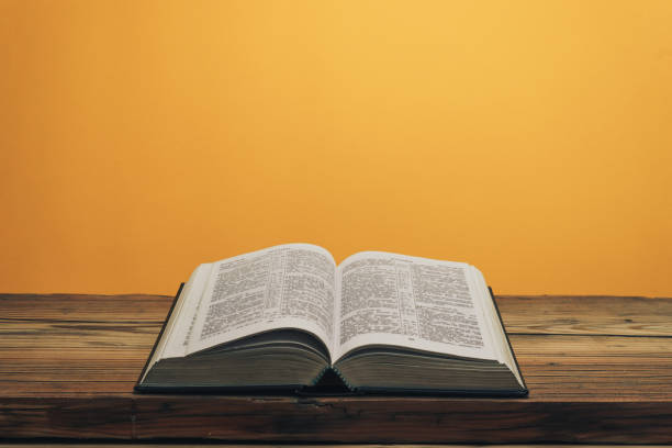 istock Open Holy Bible on a old oak wooden table. Orange wall background. 1141429018