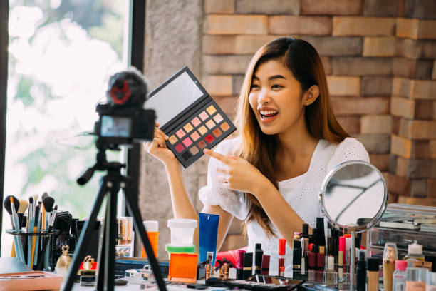 istock Pretty Asian woman recording makeup tutorial video about cosmetics with mobile phone on tripod 1141430532