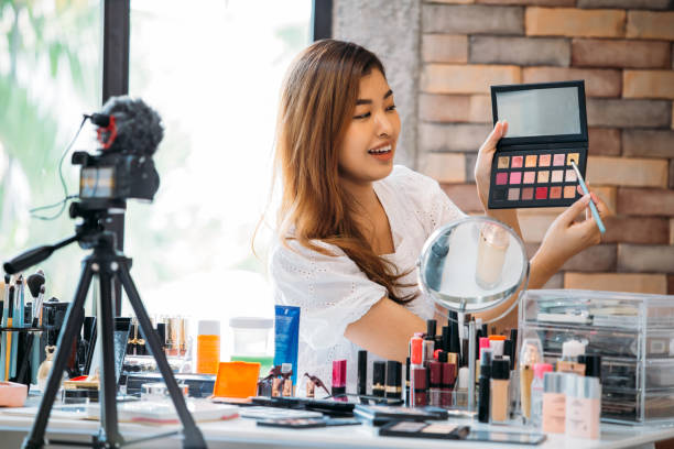 istock Pretty Asian woman recording makeup tutorial video about cosmetics with mobile phone on tripod 1141430564