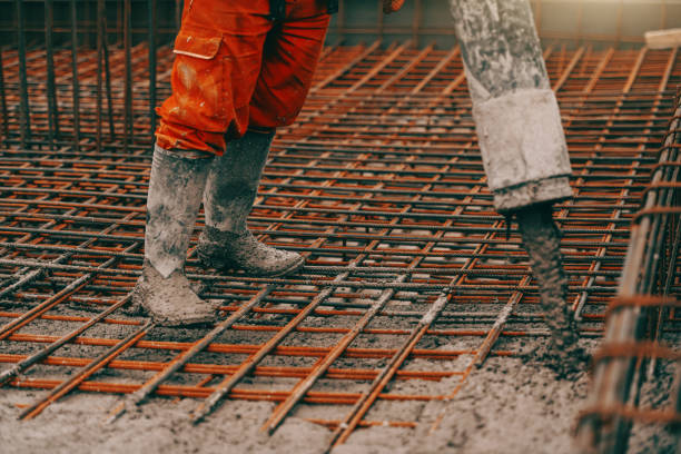 istock Construction site worker in boots and orange protective suit pouring concrete. 1141430942