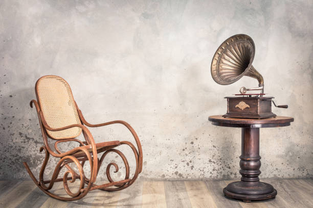 vintage antique gramophone phonograph turntable with brass horn on wooden table and aged rocking chair front concrete wall background with shadow. retro old style filtered photo - radio 1930s imagens e fotografias de stock