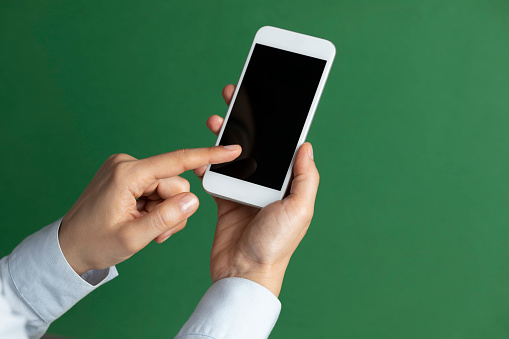 Unrecognizable person is showing screen of smart phone to camera and is pointing with one finger at device screen in front of green background.