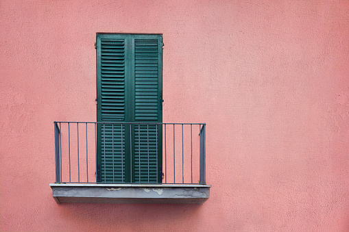 latticed wooden balcony with closed shutters on dusty rose color wall with copy space