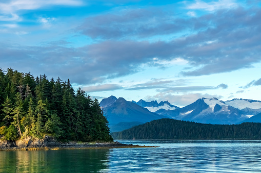 Distant snowcapped mountains in Juneau, Alaska with forest area headland in foreground.