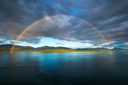 A full arched rainbow over the sea with moody sky