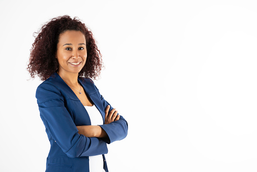 Smiling businesswoman wearing a blue jacket is looking at camera with crossed arms in front of white background.