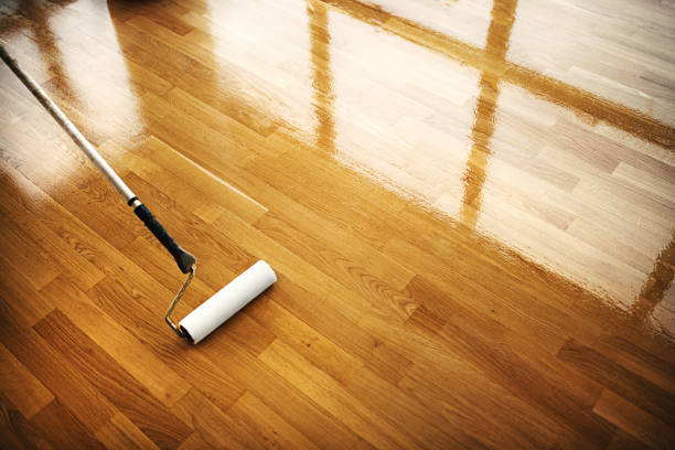 Hardwood floor restoring. Closeup top view of a solid oak floor being covered with a lacquer by using a paint roller. Shiny surface of a restored floor shows beautifully. parquet floor stock pictures, royalty-free photos & images