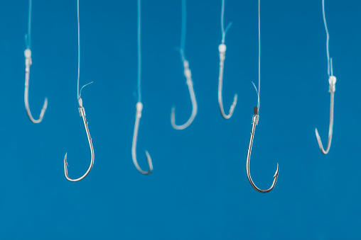 Fishing hooks are hanging with transparent string in front of blue background.