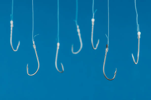 Fishing Hooks Fishing hooks are hanging with transparent string in front of blue background. hook equipment photos stock pictures, royalty-free photos & images