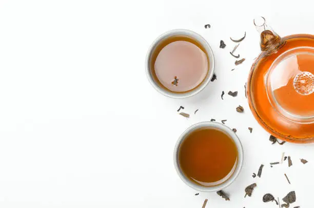 Photo of Green tea brewed in a transparent teapot and in small cups on a white table with scattered tea. Concept tea ceremony, Chinese traditions. Copy space, top view, flat lay.