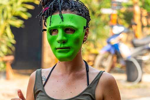 Vang Vieng, Laos - April 14, 2018: European female tourist wearing a green anonymous mask on the streets during the Lao New Year celebrations