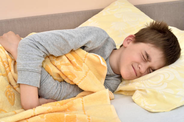 Young boy lying in bed with stomachache Ill cute young boy with closed eyes lying in bed holding his stomach one little boy stock pictures, royalty-free photos & images