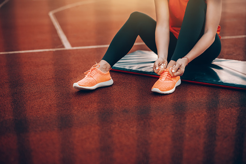 Cropped image of Caucasian woman in sportswear sitting on the mat on court and tying shoelace. Everyday is a good day to workout.