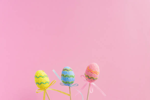 пасхальные фиолетовые, желтые и синие украшенные яйца стоят на деревянных палочках на розовом фоне. минимальная пасхальная концепция. счас - easter holiday feast day yellow стоковые фото и изображения