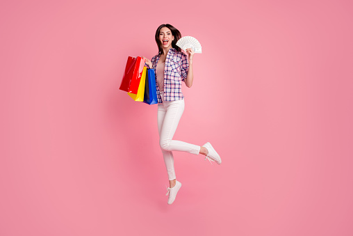 Full length side profile body size photo beautiful her she model lady jump high hold new clothes packs bucks pay wear shoes hat casual checkered plaid shirt white jeans denim isolated pink background.