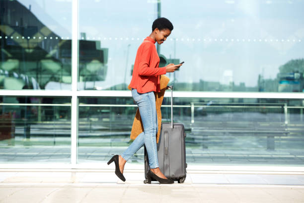 donna afroamericana che cammina con valigia e cellulare - beautiful airport women one person foto e immagini stock