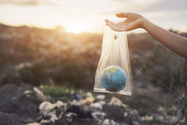 il concetto di giornata mondiale dell'ambiente. la mano della donna tiene la terra in un sacchetto di plastica su un mucchio di spazzatura nella discarica o nel backgound della discarica. concetto di inquinamento - recycled bag foto e immagini stock