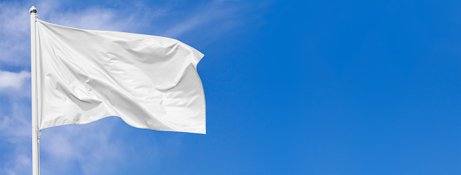 White flag waving in the wind on flagpole against the sky with clouds on sunny day, banner, closeup