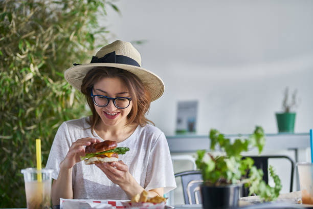 mujer sonriente feliz comiendo hamburguesa vegana sana en el restaurante de moda - hamburguesa vegetariana fotografías e imágenes de stock