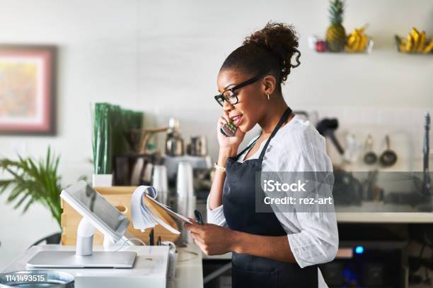 Friendly Waitress Taking Order On Phone At Restaurant And Writing On Notepad Stock Photo - Download Image Now