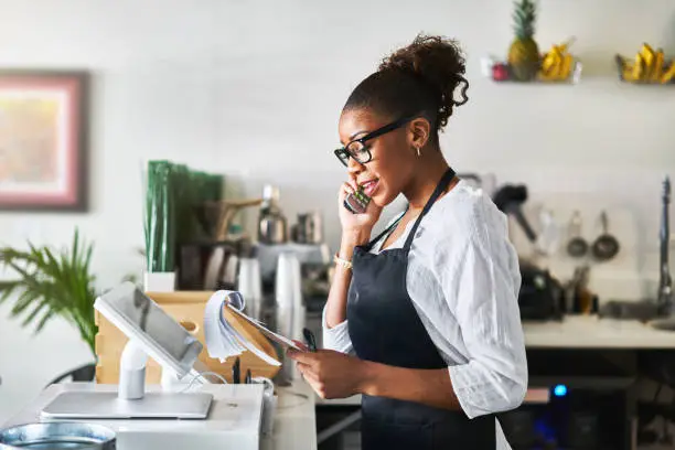 Photo of friendly waitress taking order on phone at restaurant and writing on notepad