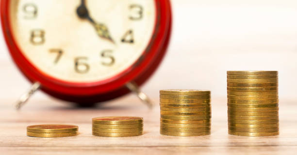 istock Spending money concept, coins with alarm clock in the background 1141494319