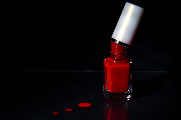 Open bottle with red nail polish. Brush touching the bottle. Drops on the table. Black background. Open bottle with red nail polish. Brush touching the bottle. Drops on the table. Black background. красота stock pictures, royalty-free photos & images