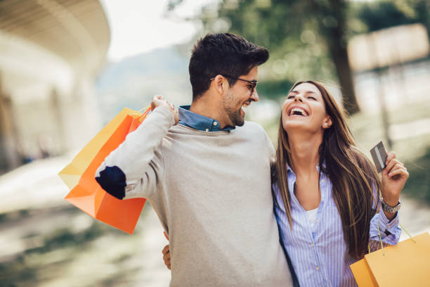 Young couple with shopping bags and credit card in the city Portrait of happy couple with shopping bags after shopping in city smiling and holding credit card credit card purchase stock pictures, royalty-free photos & images