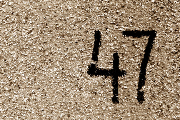 Number 47 on cement wall in stencil in brown tone.
