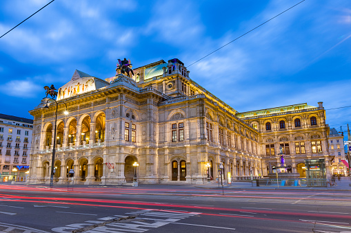 Cars pass in front of the ornate exterior of the Vienna State Opera (Wiener Staatsoper) in downtown Vienna, Austria at twilight.