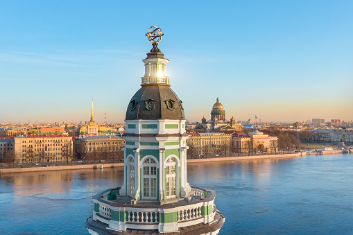 The upper part of the Kunstkamera building with an armillary sphere. View of the Neva River, the Admiralty and St. Isaac's Cathedral, in the evening, sunset at the golden hour