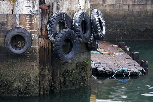 Car tyres hanging on rope against harbour wall at port dock to protect ships and boats uk