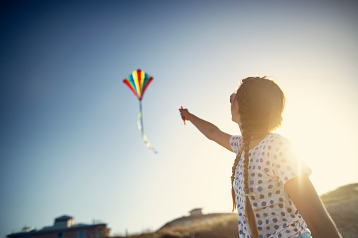 Girl enjoying flying a kite on a beach.\nNikon D850