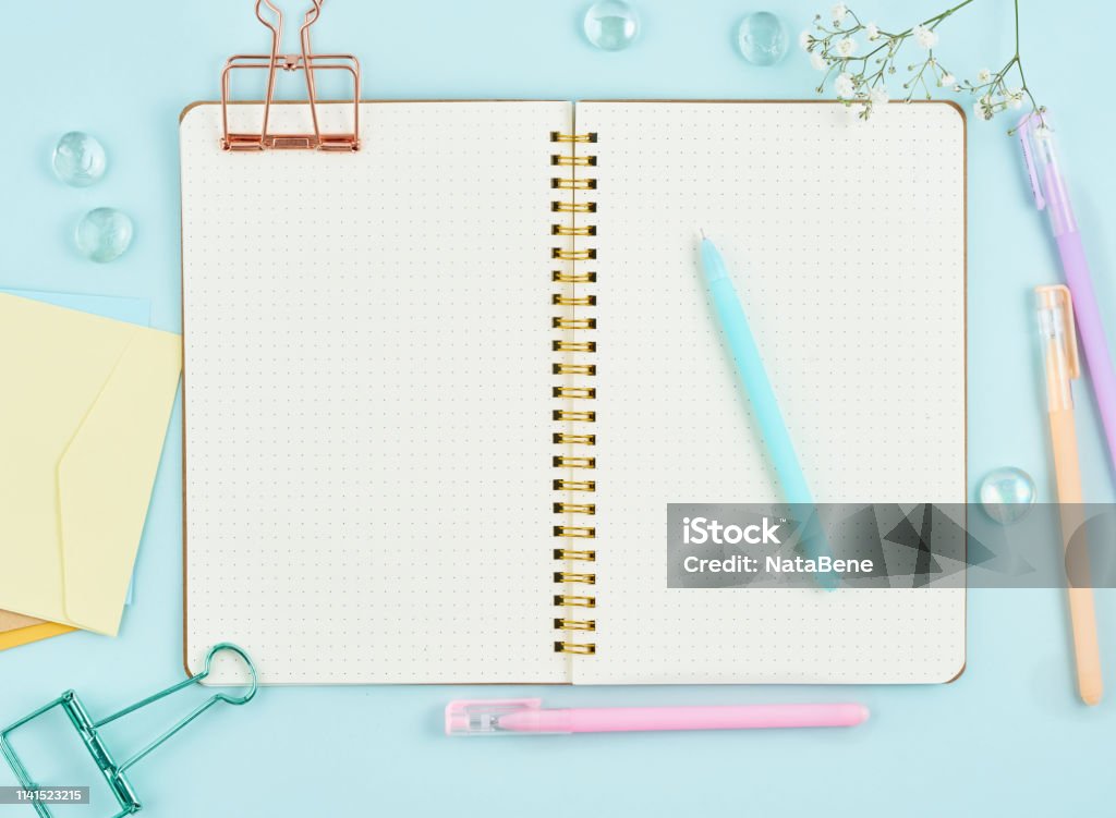 Blank notepad page in bullet journal on blue office desktop. Top view of modern bright table with notebook and flower. Mock up, copy space Blank notepad page in bullet journal on blue office desktop. Top view of modern bright table with notebook and flower. Mock up, copy space. Bullet Journal Stock Photo