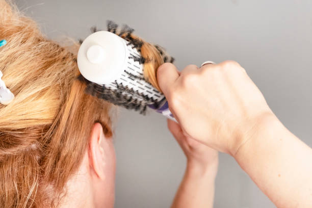 la chica endereza su cabello con un volumebrush. la reflexión en el espejo. - rizitos fotografías e imágenes de stock