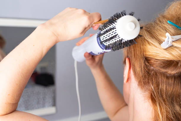 a menina endireita o cabelo com um escova-secador do volumebrush. mulher branca européia com cabelo tingido na cor vermelha. - hair care hairbrush hair dryer human hair - fotografias e filmes do acervo