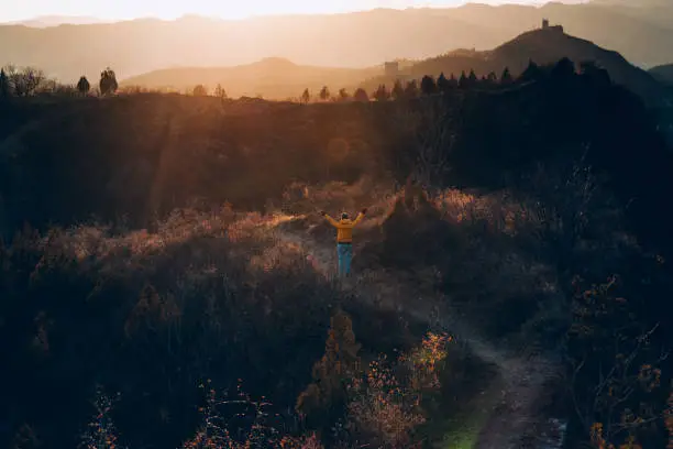 Photo of Woman hiking on mountain path from rear view raises arms to celebrate with feeling good-relax-freedom at sunset-sunrise above mountains- traveling adventure-lifestyle-outdoor activity-nature adventure