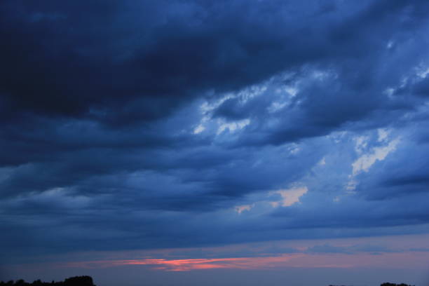 Billowy clouds roll in as the sun goes down. Lightning pokes through is electrical glow above the dark clouds.