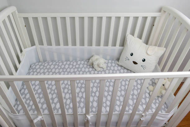 istock Looking down into empty white crib with gray sheet and cute pillow - baby‘s nursery 1141529327