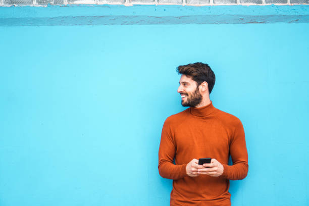 Text messaging. Smiling man leaning on the colorful wall while using mobile phone high collar stock pictures, royalty-free photos & images