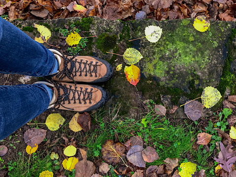 Woman in hiking boots looking down at the colorful forest floor on a rainy autumn day