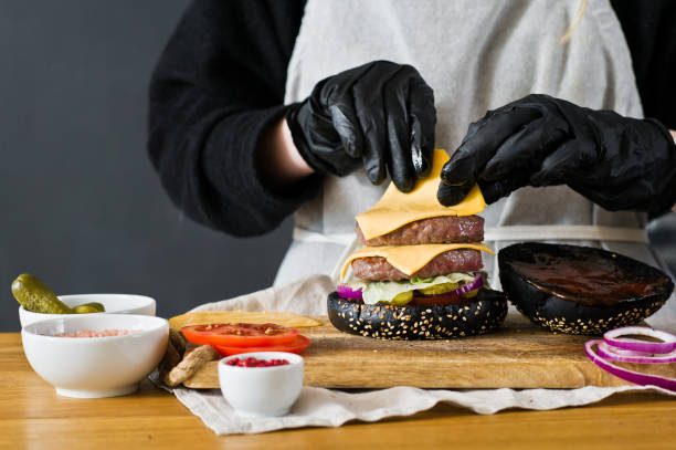 The chef prepares a huge Burger. The concept of cooking black cheeseburger. Homemade hamburger recipe. Kitchen, side view, space for text.