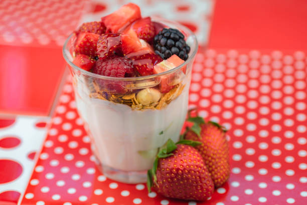 On red and white polka dot ceramic tiles, a glass with Icelandic skyr , muesli and berries (strawberries, raspberry and blackberry). Two strawberries are on the tiles by the glass. The whole subject can be seen, and it is centered.