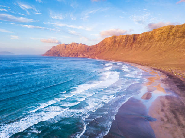 famara atlantik strand surfspot luftblick auf die landschaft von drohne auf lanzarote, kanarische inseln während des warmen sonnigen sommertages, urlaubsziel für surfen in der nähe von la santa - famara stock-fotos und bilder