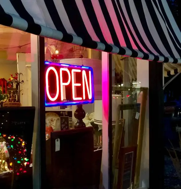 Close up view of neon open sign in the exterior of a small business featuring Christmas holiday items and a black and white awning