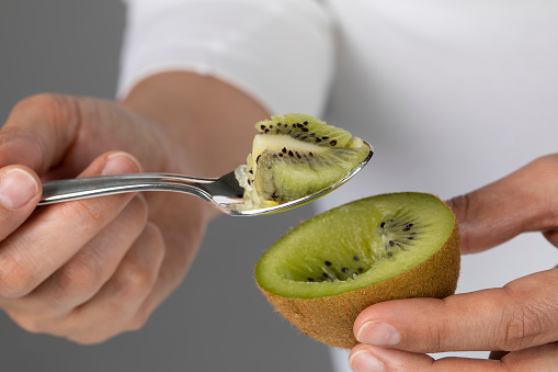 Close-up of a person eating a kiwi with a spoon.