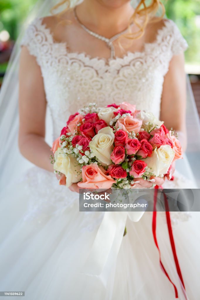La Novia En Un Vestido Blanco De La Boda Con Una Cinta Roja En Su Cinturón Con Un Ramo De Flores De Rosas En Sus Manos Foto de stock y más banco La Novia En Un Vestido Blanco De La Boda Con Una Cinta Roja En Su Cinturón Con Un Ramo De Flores De Rosas En Sus Manos Foto de stock y más banco