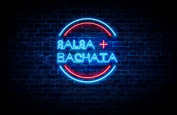 Salsa and Bachata written on a red and blue neon sign, with a brick wall in the background.
