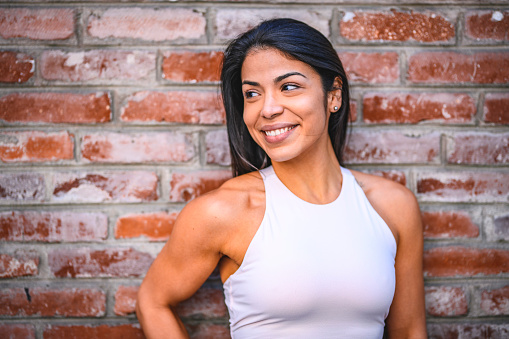 Close-up of smiling woman against brick wall. Sporty female is in sportswear. She is beautiful.
