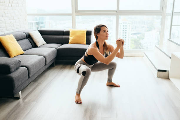 Adult Woman Training Legs Doing In and Out Squat Fit young Pacific Islander woman training at home. Beautiful female athlete working out for wellbeing in domestic gym, training legs muscles with in and out squats. woman legs open stock pictures, royalty-free photos & images